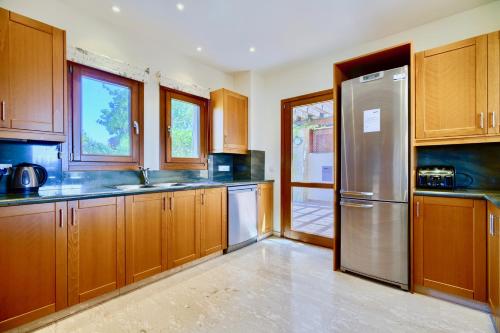 a kitchen with wooden cabinets and a stainless steel refrigerator at 4 bedroom Villa Helidoni with private infinity pool, Aphrodite Hills Resort in Kouklia