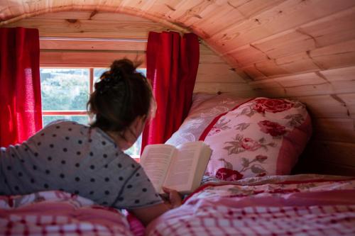 a woman laying on a bed reading a book at Camping-Erbenwald in Neubulach