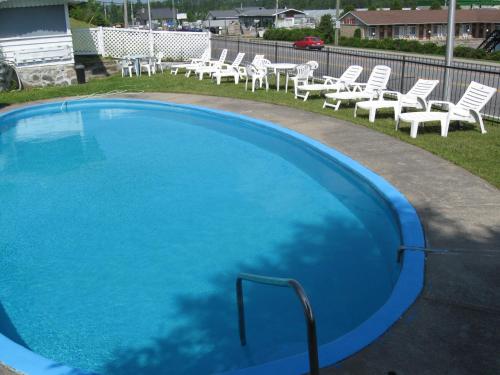 a large swimming pool with white chairs and tables at Motel Clair Mont in Sainte-Agathe-des-Monts