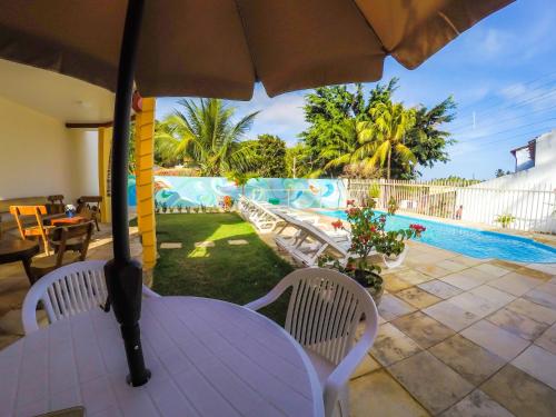 a table with an umbrella and chairs next to a pool at Flat Vila dos Milagres in São Miguel dos Milagres