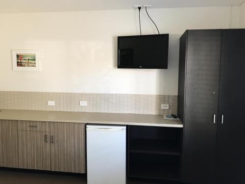 a kitchen with a white refrigerator and a tv on the wall at Thirroul Beach Motel in Wollongong