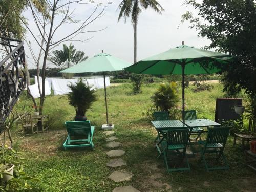 two green tables and chairs with umbrellas in a yard at The Moon River Homestay & Villa in Hoi An