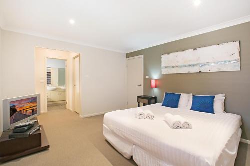 a bedroom with a large white bed and a flat screen tv at Peppertree Lodge Hunter Valley in Rothbury