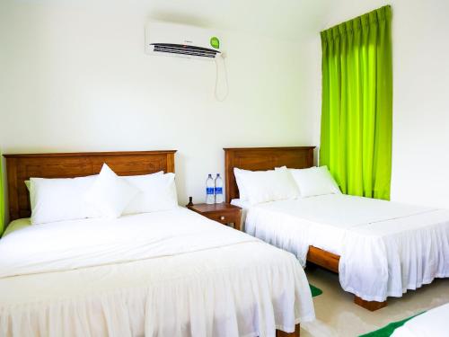 two beds in a room with green curtains at Pasikudah Eco Village Hotel in Pasikuda