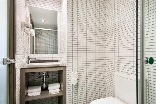 a white tiled bathroom with a sink and a toilet at Hotel Acta Laumon in Barcelona