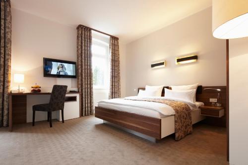 a hotel room with a bed and a desk and a television at Bielefelder Berghotel zum Stillen Frieden in Bielefeld