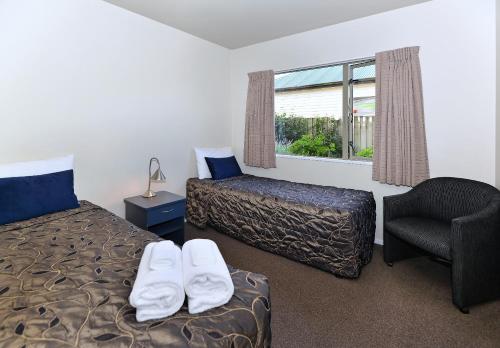 een slaapkamer met 2 bedden, een stoel en een raam bij Arena Motel in Christchurch