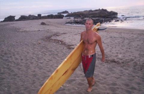 a man holding a surfboard on the beach at Playa Roca Beach Hotel in Las Peñitas