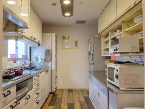 広島市にあるジェイホッパーズ広島ゲストハウスのキッチン(白いキャビネット、冷蔵庫付)