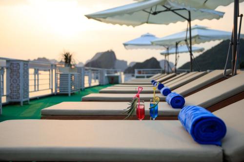a row of lounge chairs with drinks and umbrellas at Alisa Premier Cruise in Ha Long