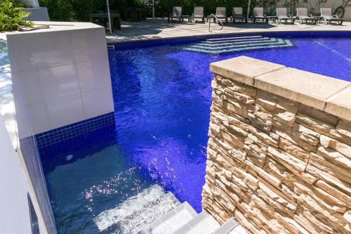 a pool with blue water and a stone wall at Grand Mercure Allegra Hervey Bay in Hervey Bay