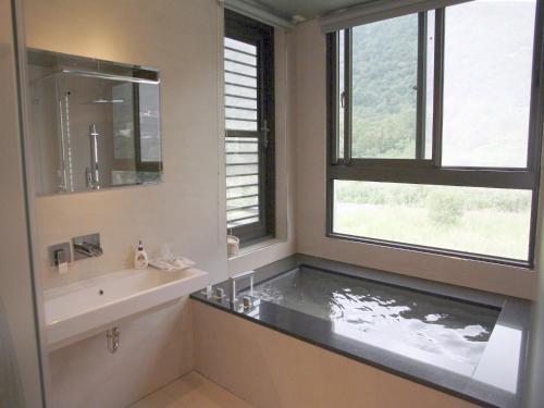 a bathroom with a tub and a sink and two windows at Peace Area Hot Spring Hotel in Jiaoxi