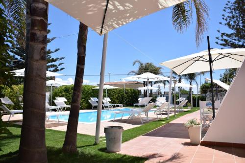 a swimming pool with umbrellas and chairs next to a resort at Villa Blanche Dimora Di Charme in Marsala