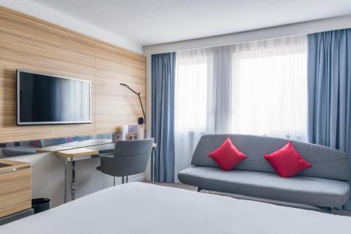 a hotel room with a bed and a couch and a television at Novotel Strasbourg Centre Halles in Strasbourg