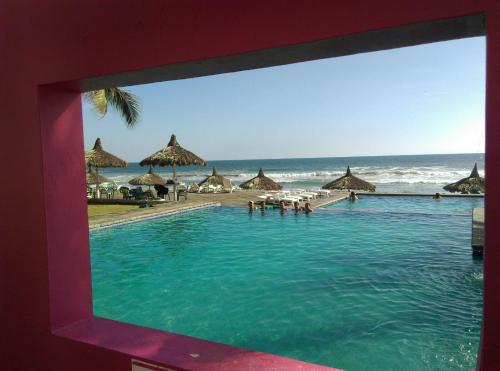 a swimming pool next to a beach with umbrellas at Apartamento en la playa en Mazatlán in Mazatlán