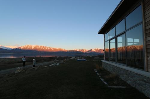 a person standing next to a house with mountains in the background at Isolation Bay in Lake Tekapo