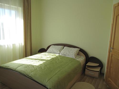 a bedroom with a bed with a green blanket and a window at Vila Laima in Šventoji