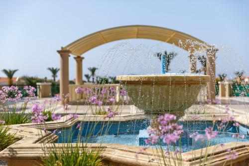 a fountain in a garden with purple flowers at Lindos Princess Beach Hotel in Lardos