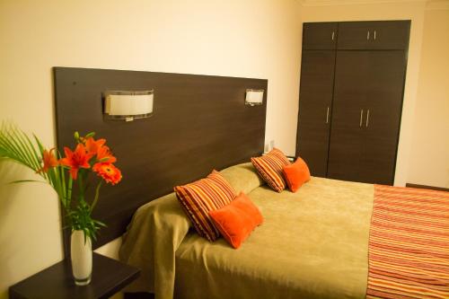 1 dormitorio con 1 cama con almohadas de color naranja y un jarrón de flores en Hotel Las Vegas en Salta