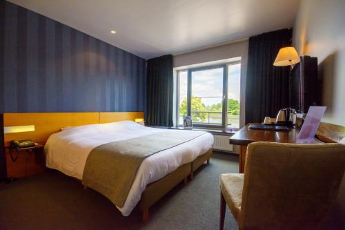 een hotelkamer met een bed, een bureau en een raam bij Hotel Sirius in Huy