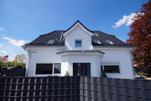 a white house with a black roof behind a black fence at Pension / Zimmervermietung Wasbek in Wasbek