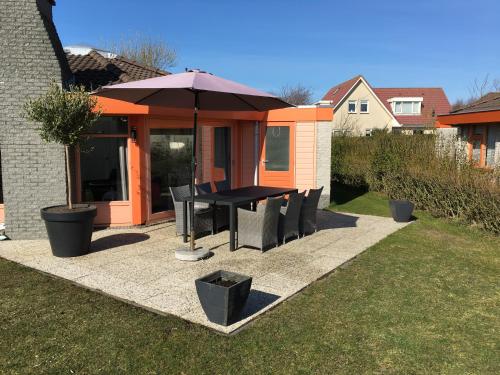 a patio with a table and chairs and an umbrella at Ferienhaus am Meer mit Kamin & Sauna - Seestern 251 in Julianadorp