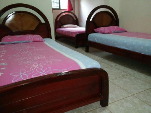three beds in a room with pink and purple sheets at Hotel Boston in Guayaquil