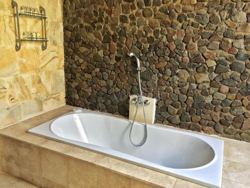 a bath tub in a bathroom with a stone wall at Puri Mas Boutique Resort & Spa in Senggigi 