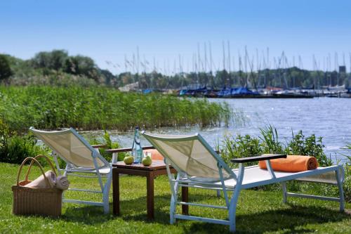 two chairs and a table next to a body of water at Romantik Hotel Jagdhaus Eiden am See in Bad Zwischenahn