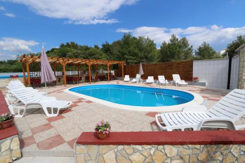 ein Pool mit weißen Stühlen und einem Haufen von Plätzen in der Unterkunft Pansion Comfort Sidro in Novalja