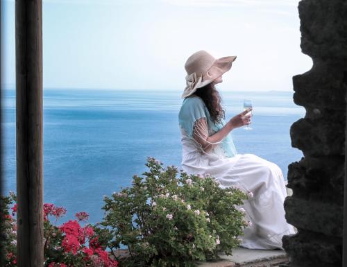 a woman sitting on a ledge looking at a cell phone at Aegean Castle Andros – Adults Only in Agia Eleousa