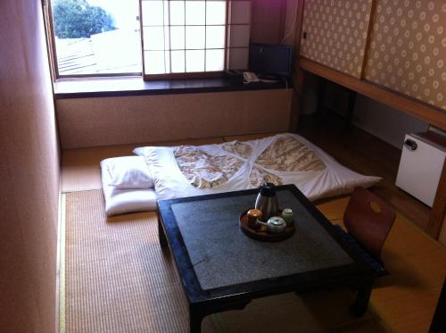 a small room with a bed and a table and a window at Kamesei Ryokan in Chikuma