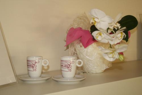 two coffee cups on a shelf with a bag of flowers at Art Hotel Udine in Udine