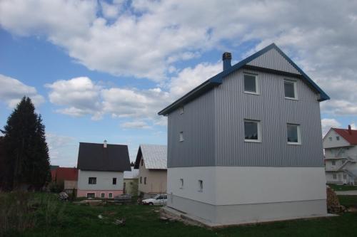a white house with a gray roof on a yard at Apartman Lucija in Žabljak