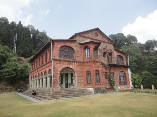 a large brick building with a grass field in front at Raghu Vilas in Mussoorie