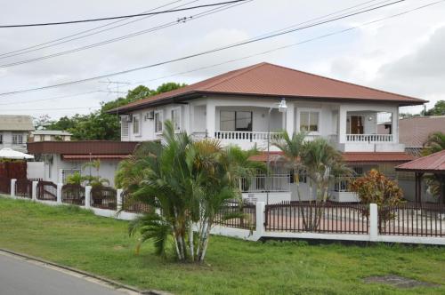 a white house with a red roof and palm trees at Riando appartement in Paramaribo
