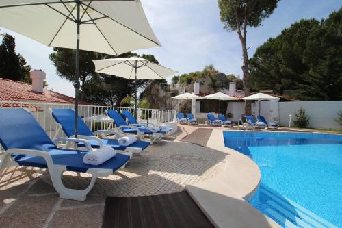 a pool with blue chairs and umbrellas next to a swimming pool at Villa Branca do Castelo in Sesimbra