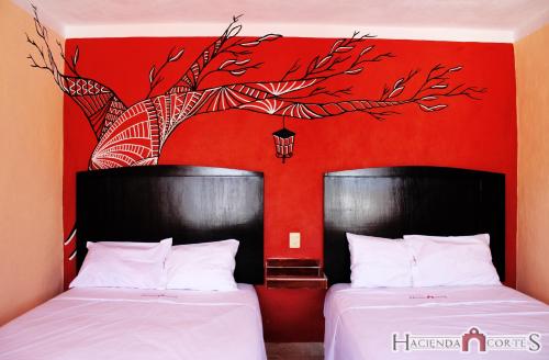 2 camas en una habitación con una pared roja en Hotel Hacienda Cortes en Mérida