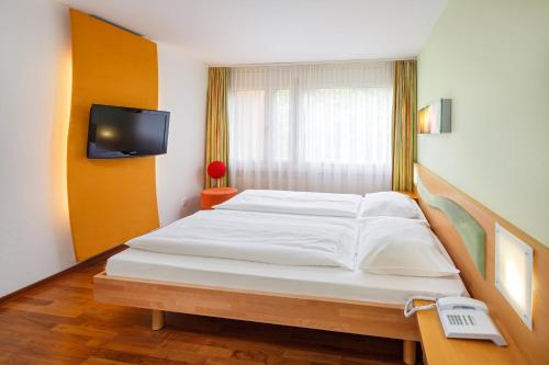 a bedroom with a large white bed with a television at Ramada by Wyndham Baden Hotel du Parc in Baden