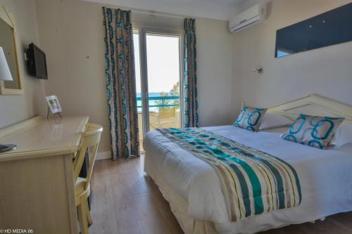 a bedroom with a bed and a desk and a window at Hôtel Méditerranée in Le Lavandou