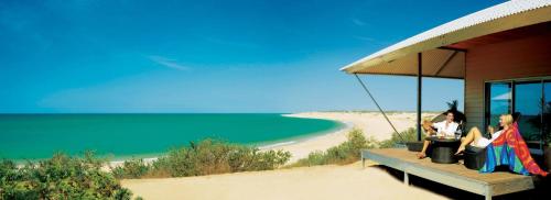 two people sitting on a porch on a beach at Eco Beach Wilderness Retreat in Broome