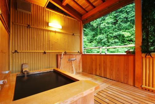 a large tub in a wooden room with a window at Shoenso Hozugawatei in Kameoka