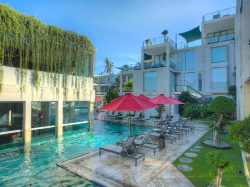 a pool with chairs and umbrellas in front of a building at FuramaXclusive Ocean Beach Seminyak Bali in Legian