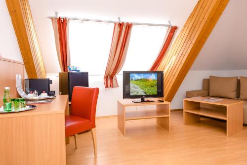 a living room with a desk with a television and a chair at Stadthotel Schwerterbräu in Judenburg