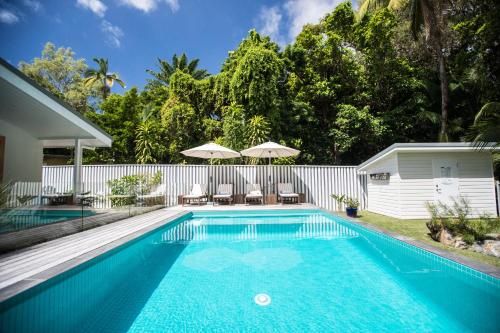 a pool with chairs and umbrellas next to a house at Pineapple Petes Beach House in Port Douglas