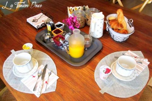 una mesa con una bandeja de alimentos para el desayuno y zumo de naranja en La Taniere Douce, en Soulaucourt-sur-Mouzon