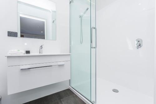 uma casa de banho branca com uma cabina de duche em vidro. em Superior Dunedin Apartments em Dunedin