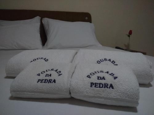 a bed with white towels with the words days my dadana va pedra at Pousada da Pedra in Delmiro Gouveia