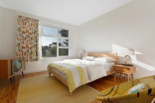 a white bedroom with a bed and a television at The 50's Beach House in Merimbula