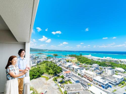 a couple standing on a balcony looking out at the ocean at Kanehide Onna Marine View Palace in Onna
